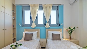 A double room with two beds, a small bedside table with a vase of flowers, and a window with curtains. - Bessie's dream Villa (Rethymno)