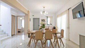 A dining area with a marble floor, wooden chairs, a table with a vase of flowers, and a television mounted on the wall. - Bessie's dream Villa (Rethymno)