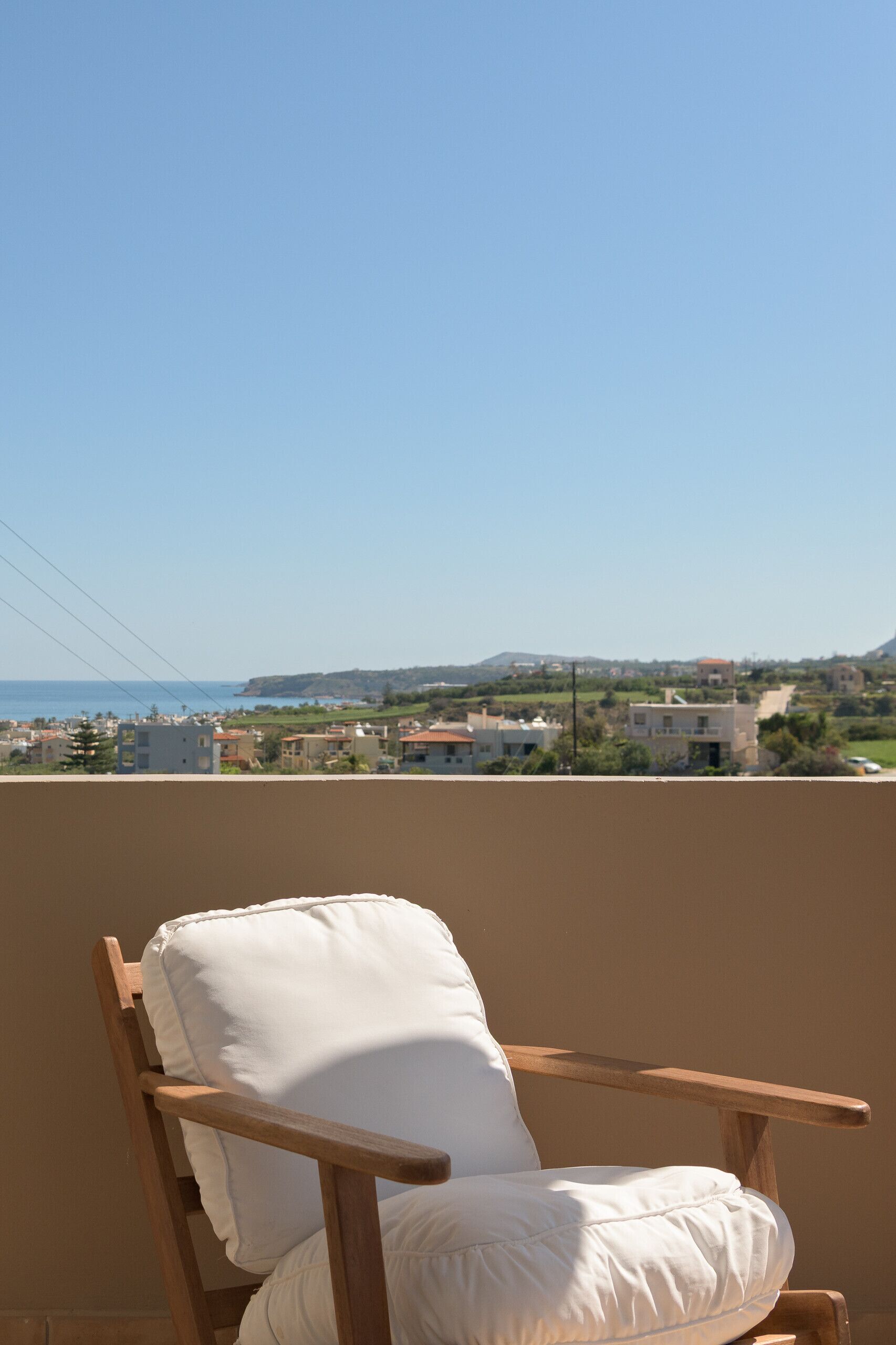 A wooden chair with a white cushion on a balcony overlooking a coastal town.
