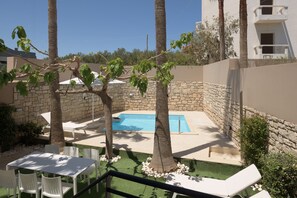 Un espace piscine agrémenté d’un mur en pierre, de palmiers et d’une table blanche avec des chaises.