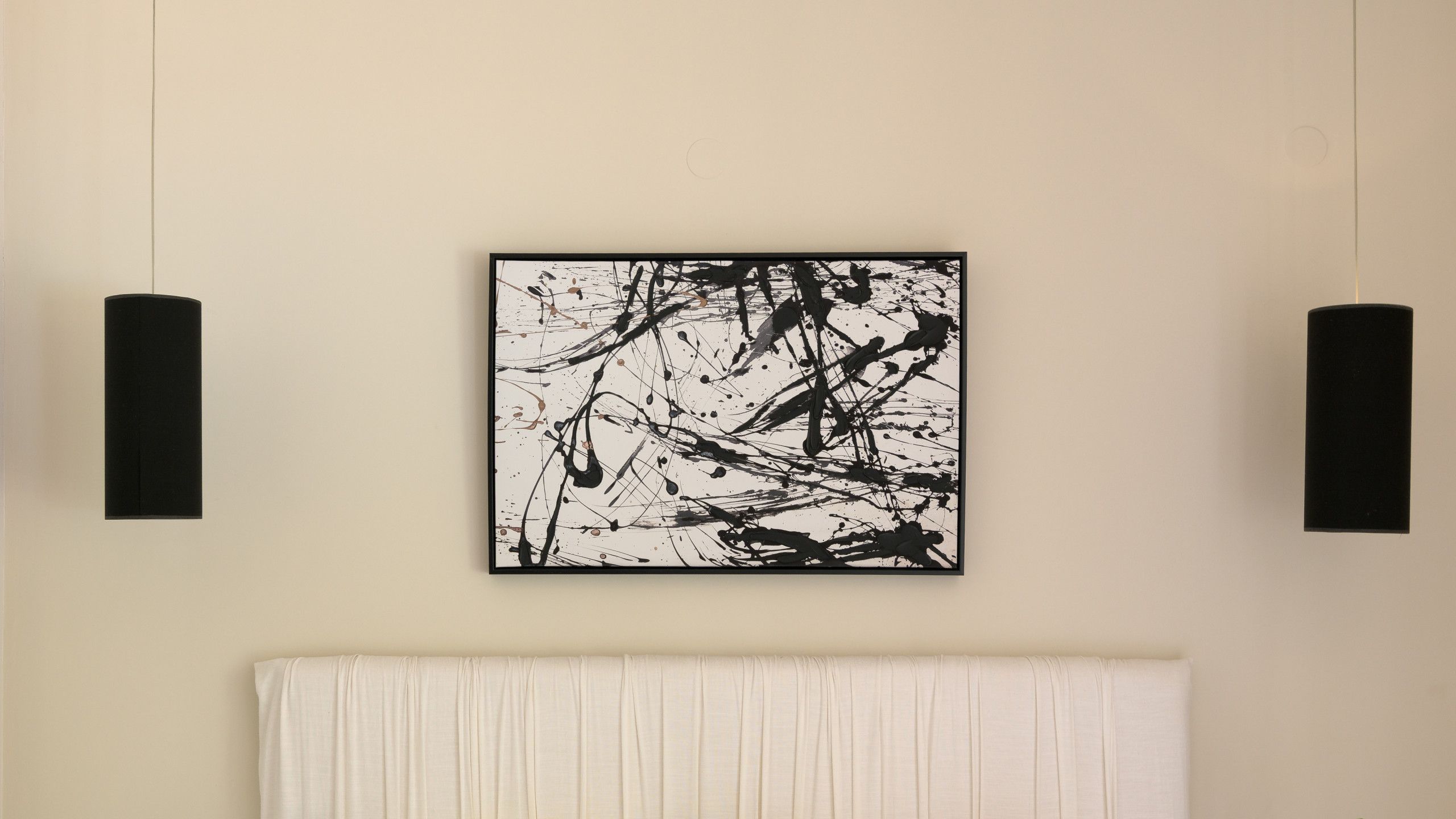 A room with a painting on the wall, a white curtain, and two black wall sconces.