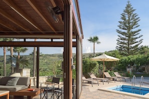 A covered outdoor area with a pool, lounge chairs, and a view of the surrounding landscape.