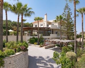 A modern villa with a stone wall, a pergola, and lush greenery.
