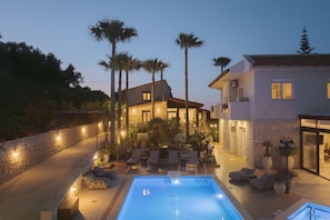 A poolside area with lounge chairs, a swimming pool, and a building with a stone facade and palm trees.
