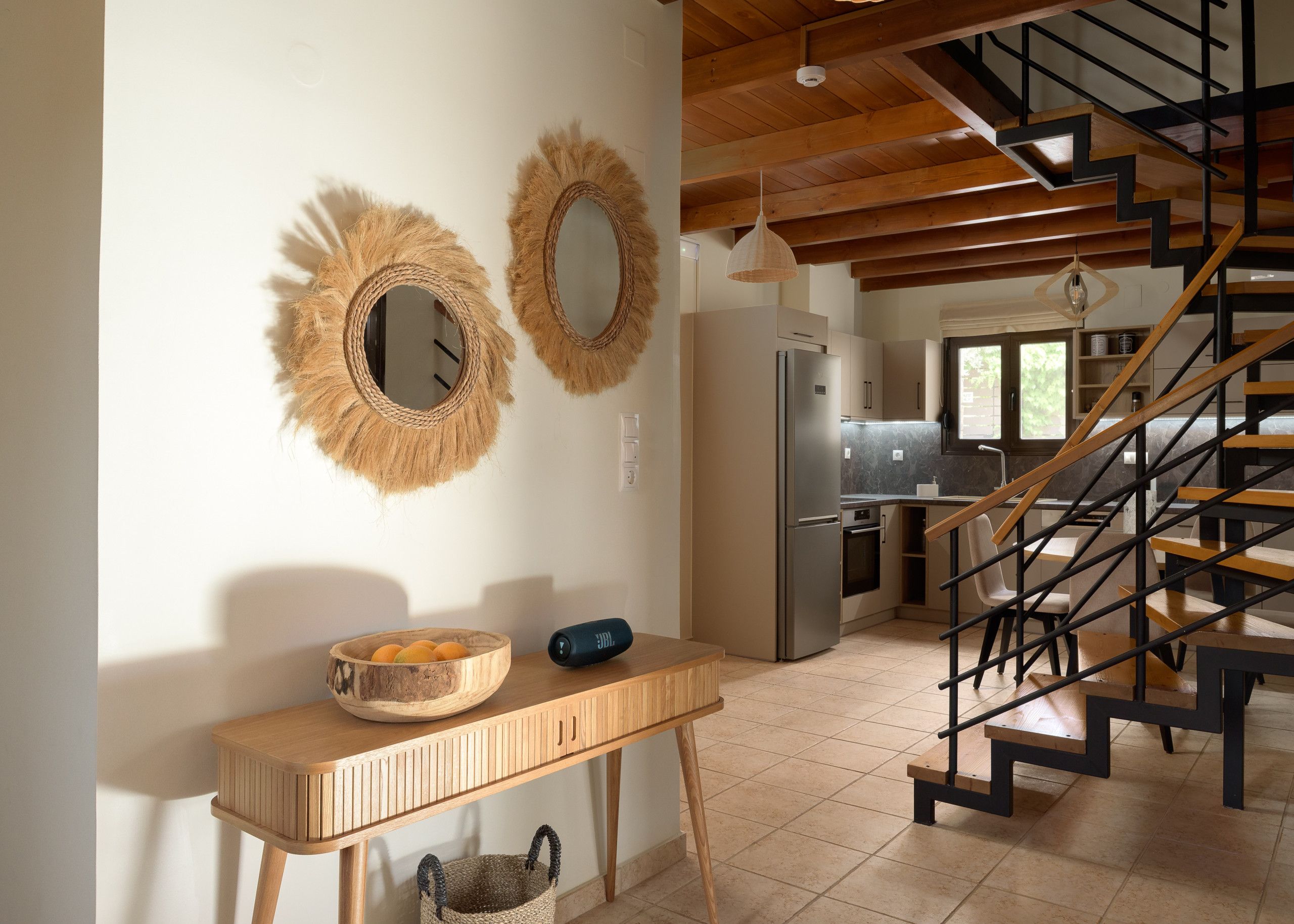 Une cuisine avec une table en bois, deux miroirs fixés au mur, un réfrigérateur et un escalier avec des marches en bois.