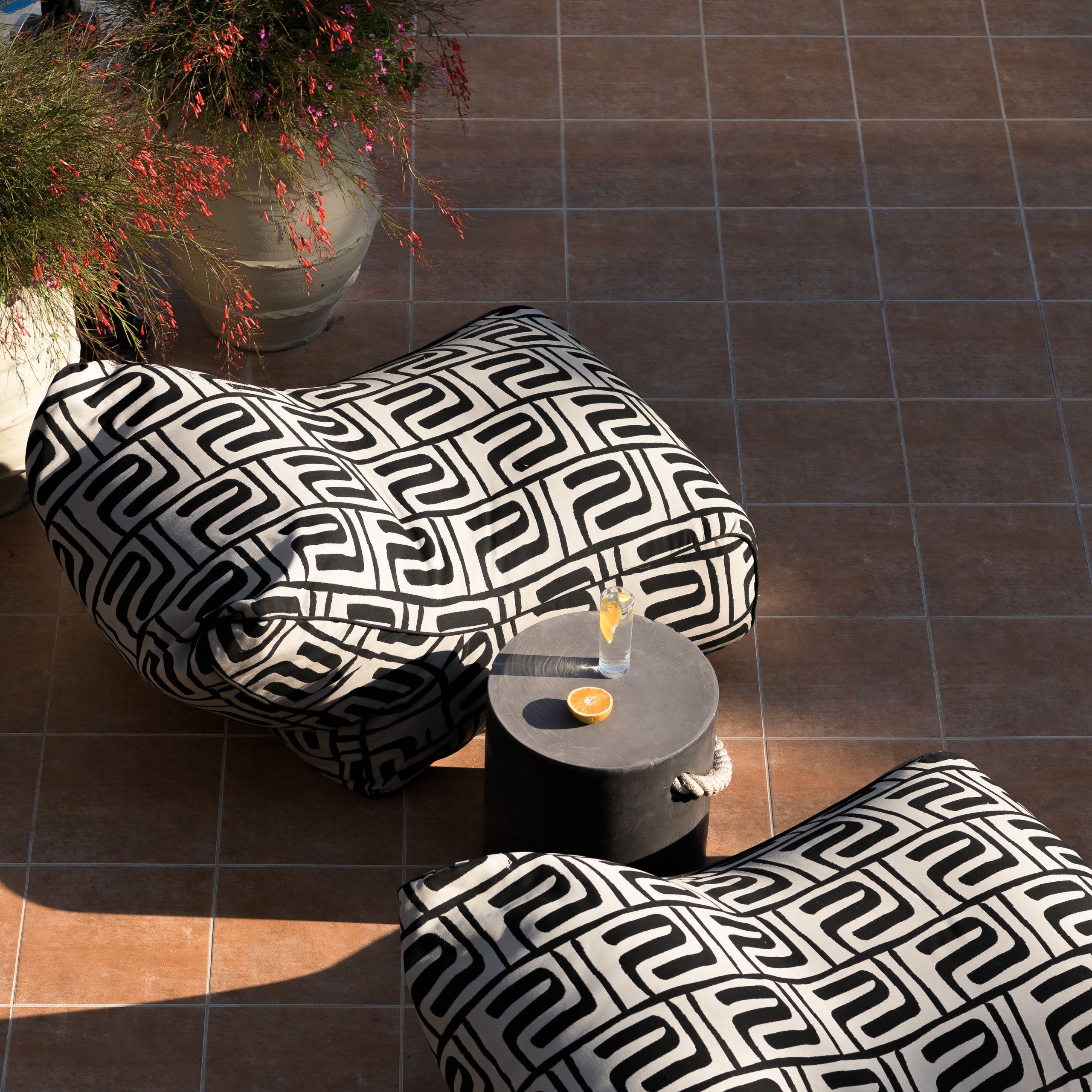 A tiled patio area with two patterned cushions and a small round table with a drink and an orange slice.