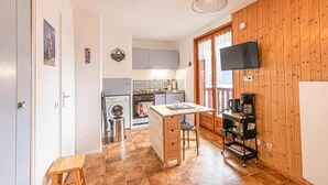 Een compacte keuken met een wasmachine, een eettafel en een aan de muur bevestigde televisie.