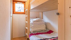 Een kleine kamer met een stapelbed, een klein raam en een deur.