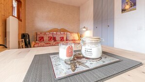 Een knus vertrek met een houten plafond, een gestreept sofa, een tafel met een kaars en pot, en een muur met een poster.