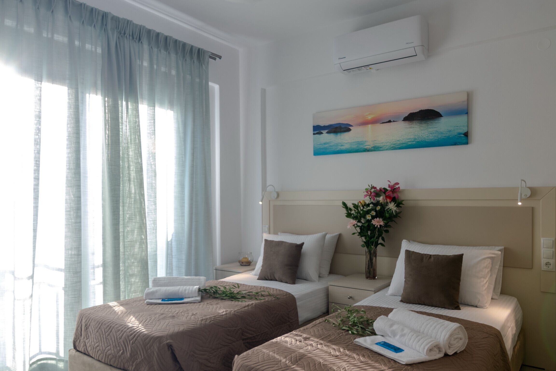 A hotel room with two beds, a painting of a sunset over water, and an air conditioning unit on the wall.