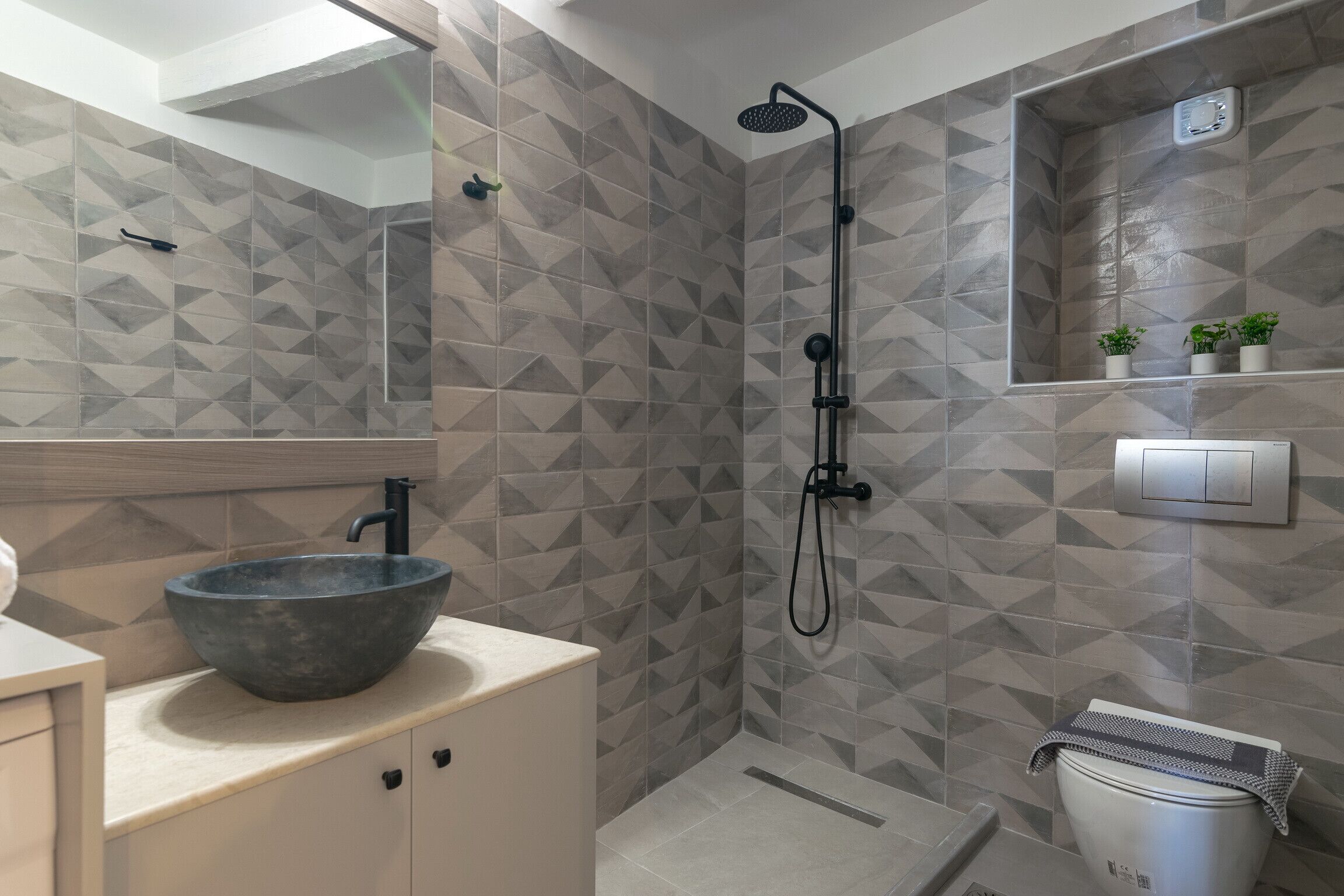 Un bagno moderno con un motivo a piastrelle geometriche, un lavabo a colonna, un soffione doccia manuale e un water con un asciugamano sopra.
