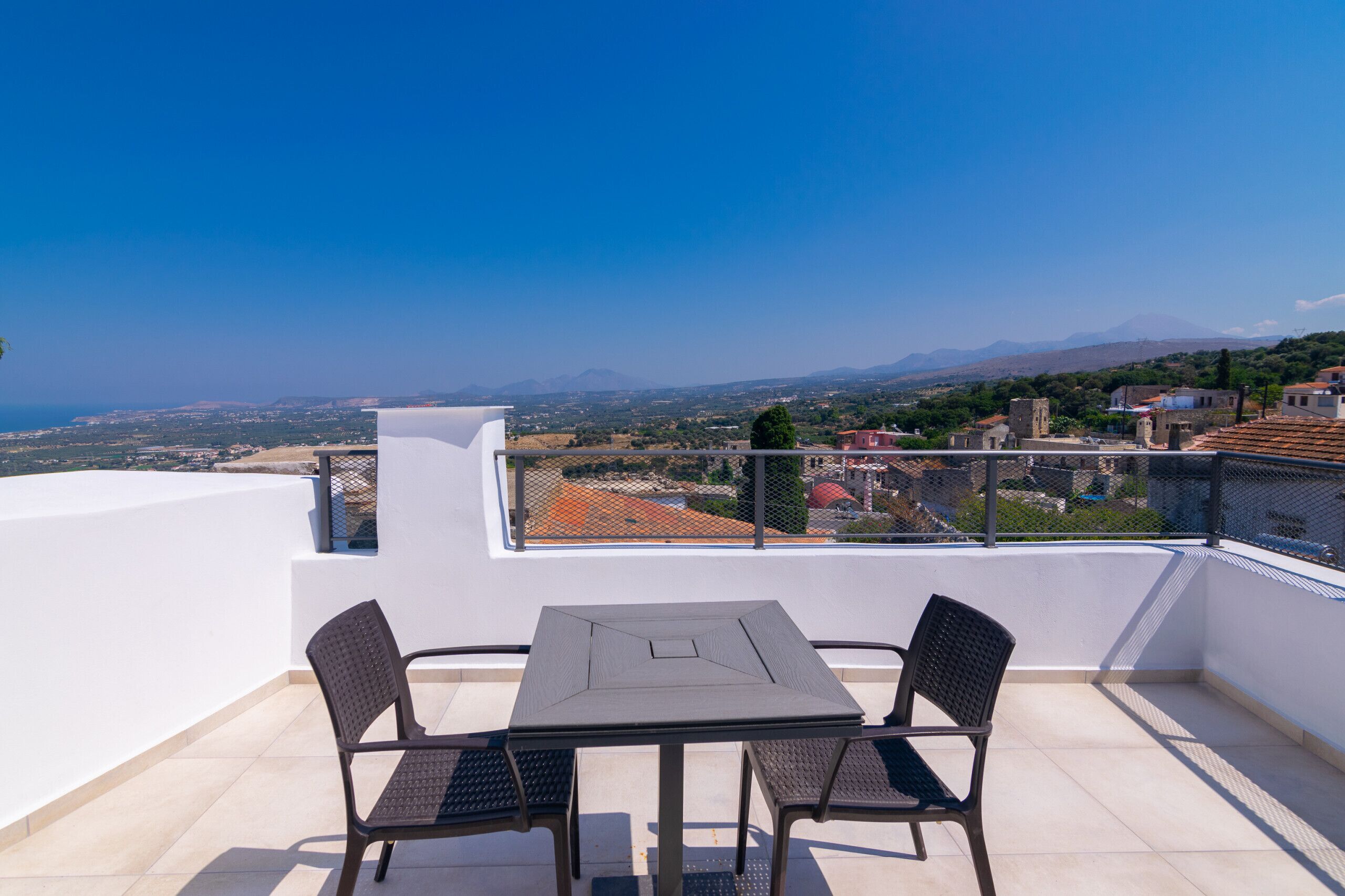 Un balcon avec une table et des chaises, offrant une vue panoramique sur la ville et les montagnes.