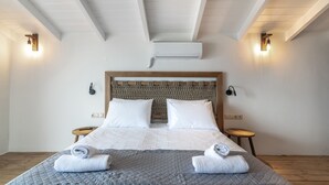 Un lit bien fait, avec du linge de lit blanc et gris, deux tables de chevet avec des lampes et une tête de lit en bois.