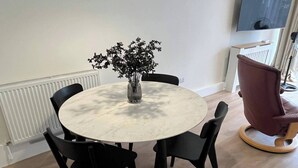 A round table with a marble top surrounded by four black chairs. A vase with flowers is placed on the table. - Cozy Cromwell Cottage in Croydon (Croydon)