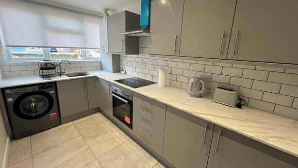 A modern kitchen with grey cabinets, a built-in oven, a washing machine, and a window with a view of the outside. - Cozy Cromwell Cottage in Croydon (Croydon)