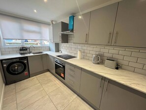 Una cucina moderna con mobili grigi, forno integrato, lavatrice e finestra con vista esterna.