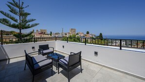 A rooftop terrace with outdoor furniture, a view of the sea, and buildings in the background. - View Mare Maroulas Villa (Rethymno)
