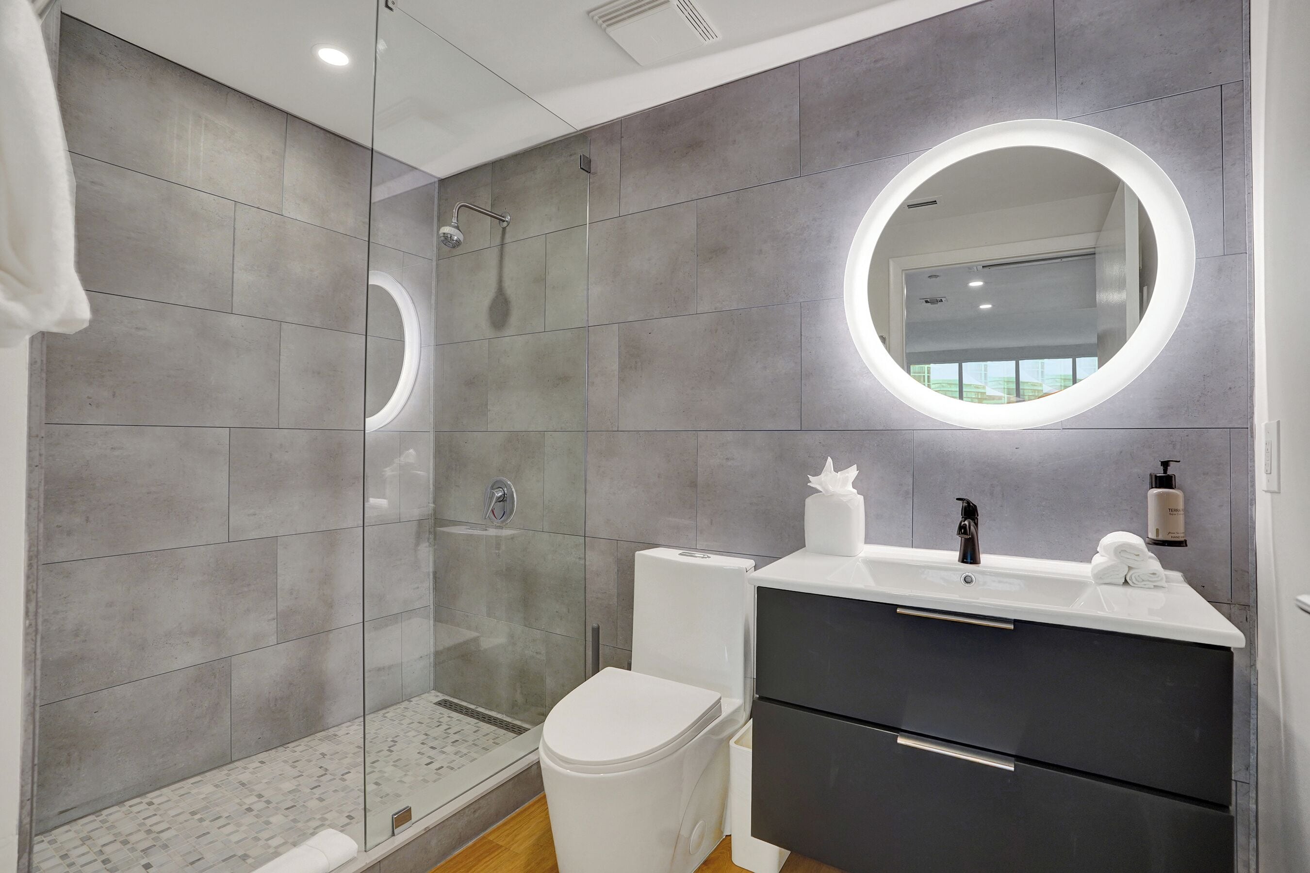A modern bathroom with a glass-enclosed shower, a white toilet, a vanity with a mirror, and a towel on the counter.