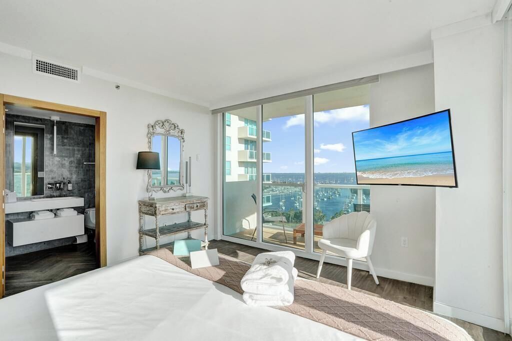 A modern hotel room with a large bed, a bathroom with a vanity, a television mounted on the wall, and a balcony with a city view.