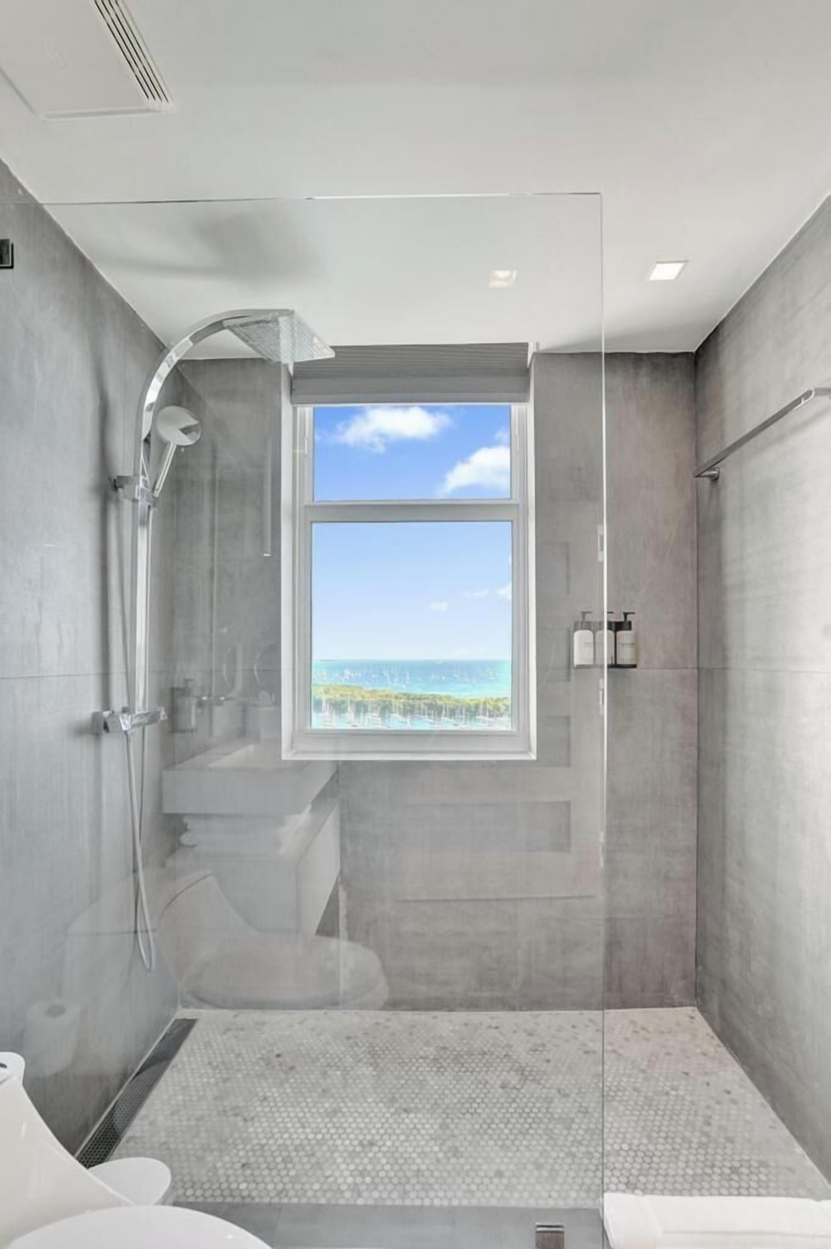 A modern bathroom with a glass-enclosed shower, a view of the ocean, and a minimalist design.