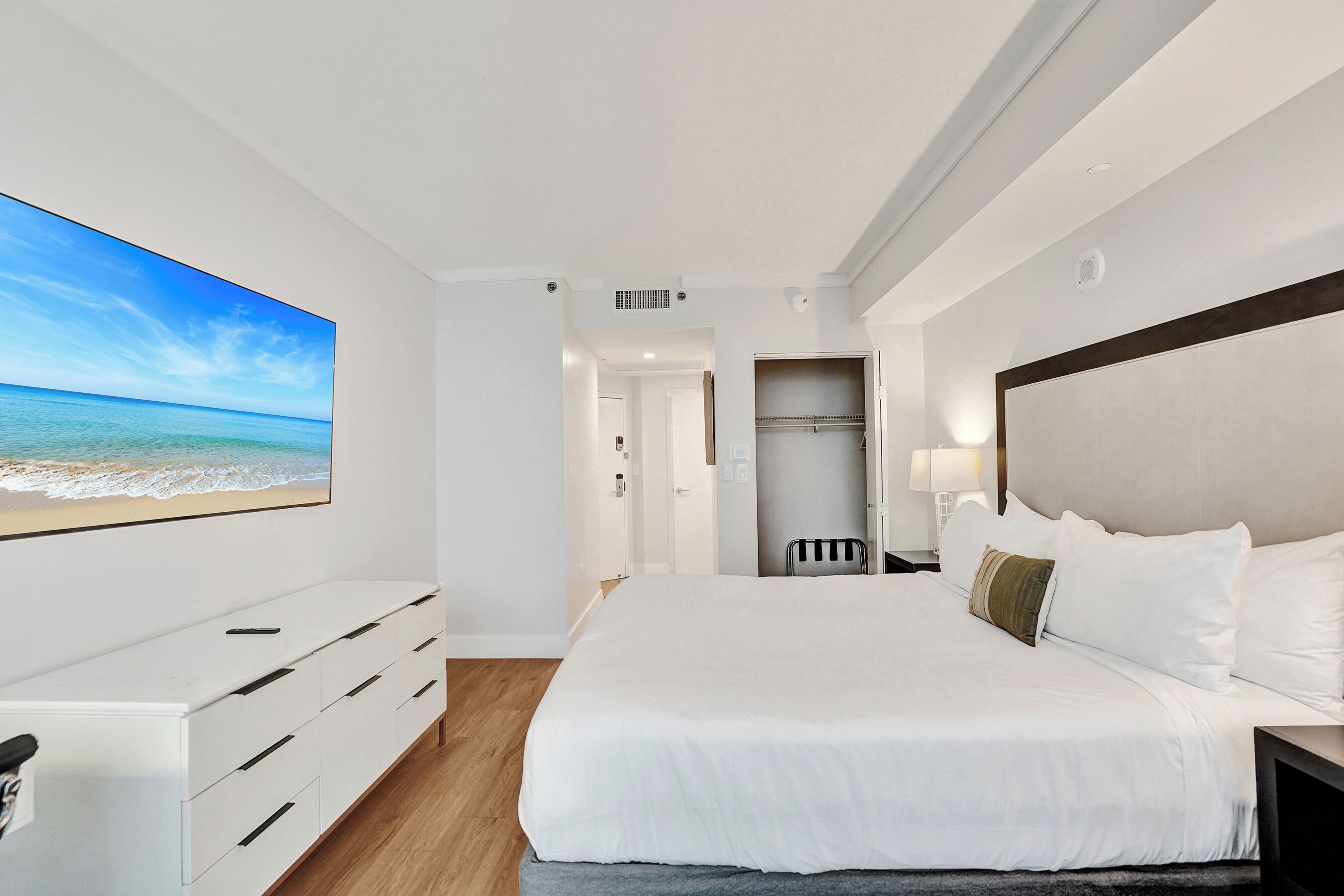 Habitación de hotel con una cama grande, un tocador blanco, un armario y vista a la playa.