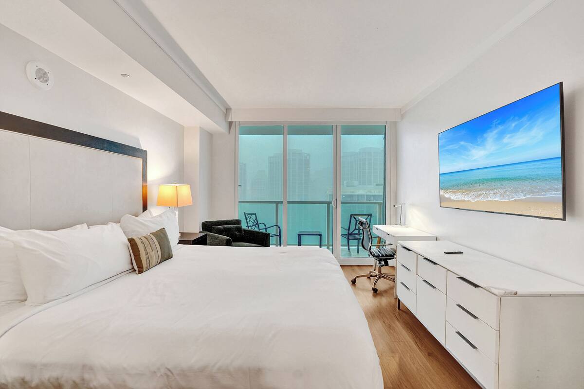 A hotel room with a large bed, a desk, a chair, and a TV on the wall.