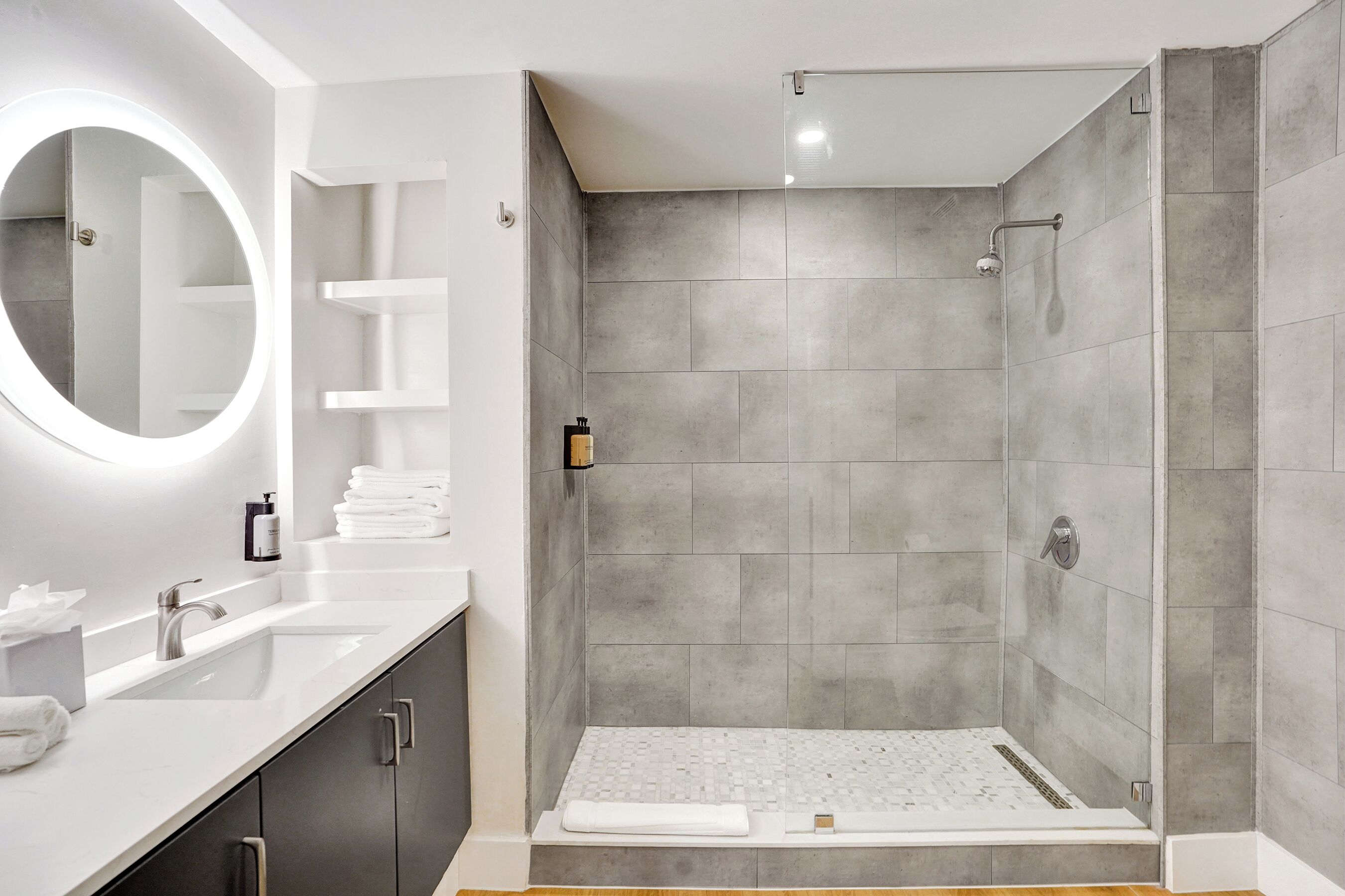 A modern bathroom with a shower, a sink, a mirror, and a toilet.