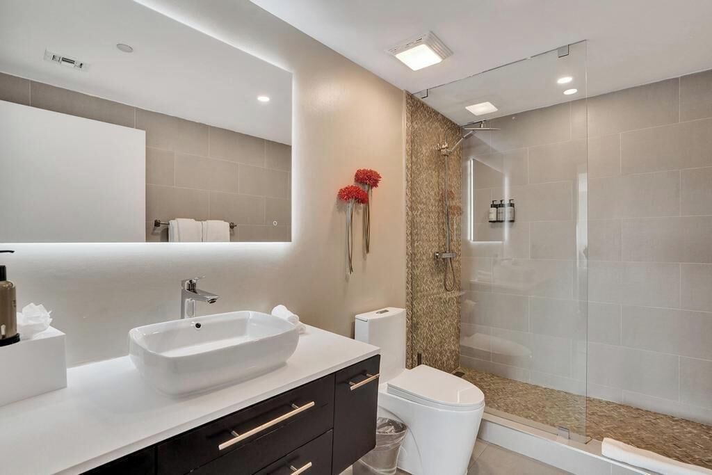 A modern bathroom with a large white sink, dark cabinets, a toilet, and a glass-enclosed shower.