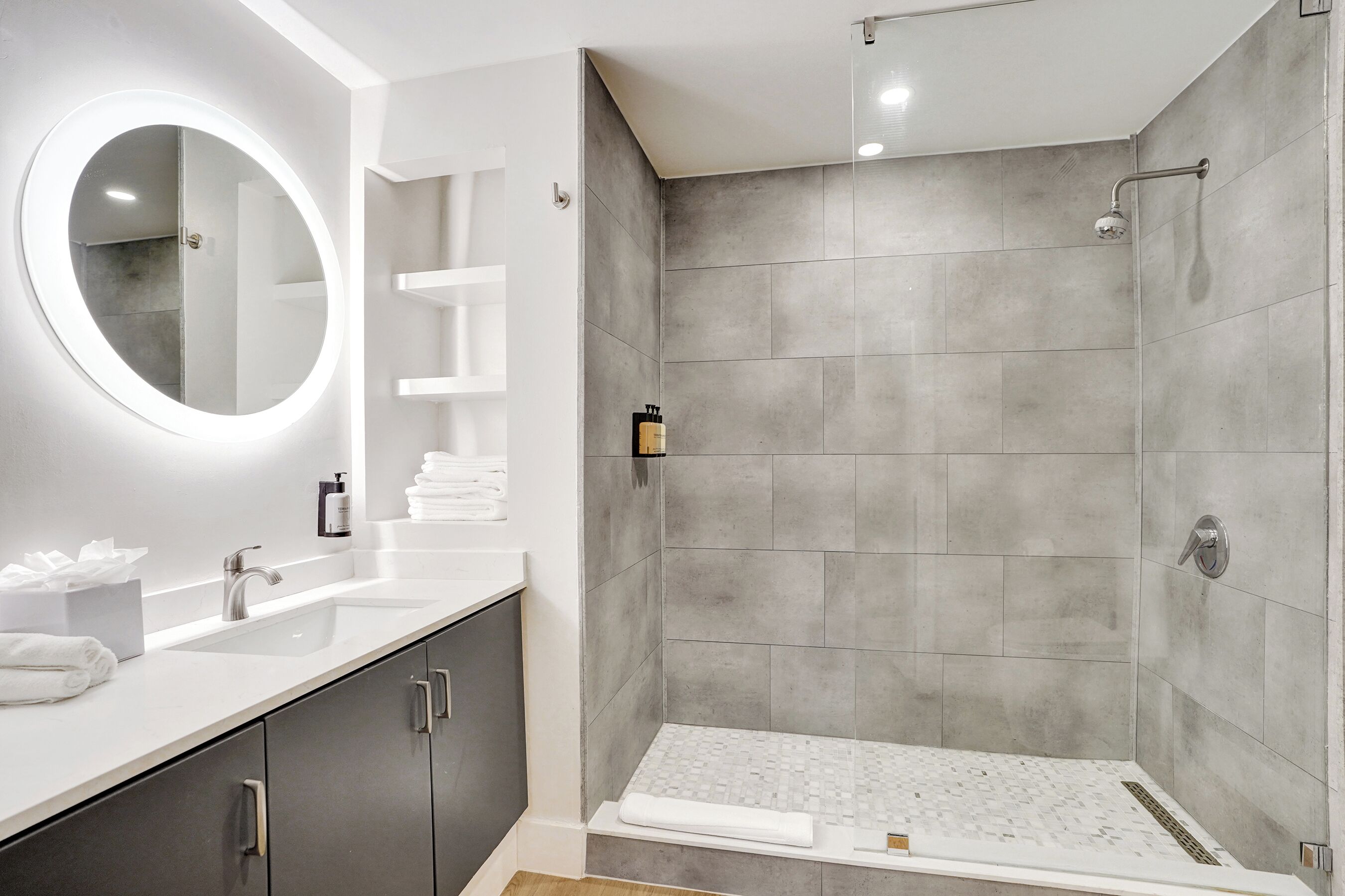 A modern bathroom with a large mirror, two sinks, a shower, and a tiled floor.