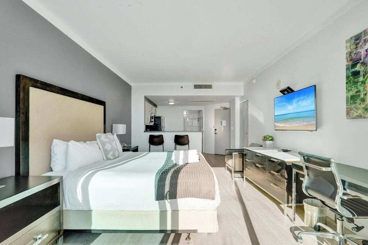 A modern hotel room with a large bed, a desk, and a view of the sea.