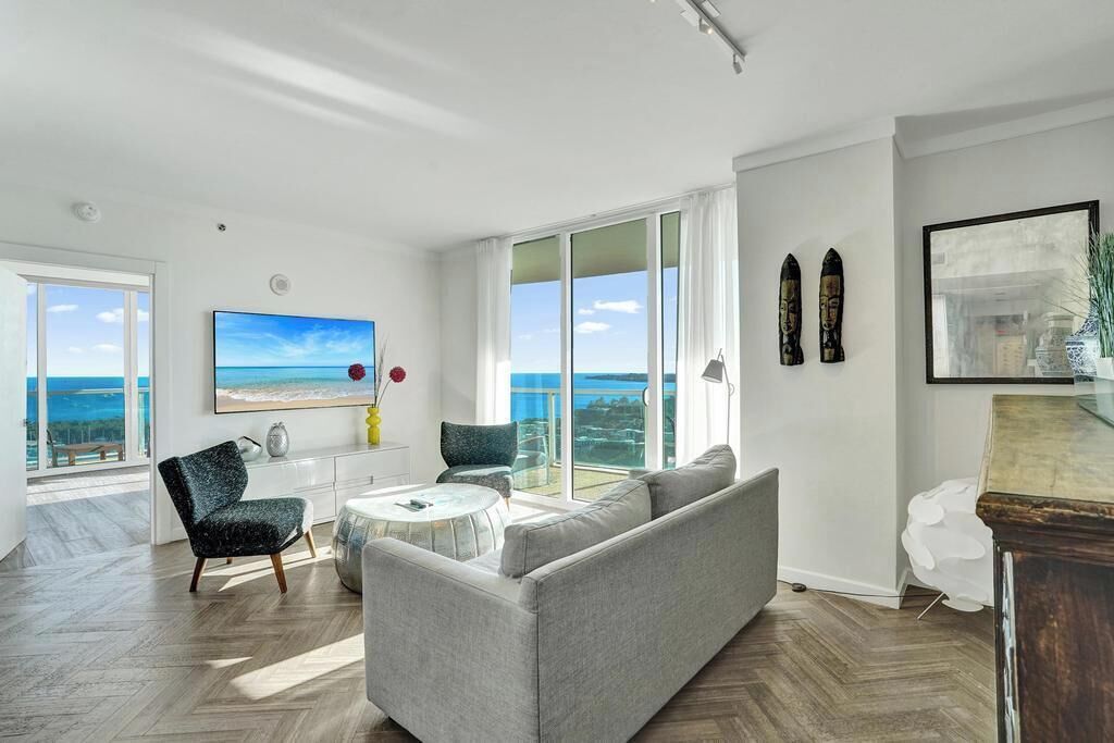 Una sala de estar moderna con un gran ventanal, un sofá, un sillón y una mesa de centro.