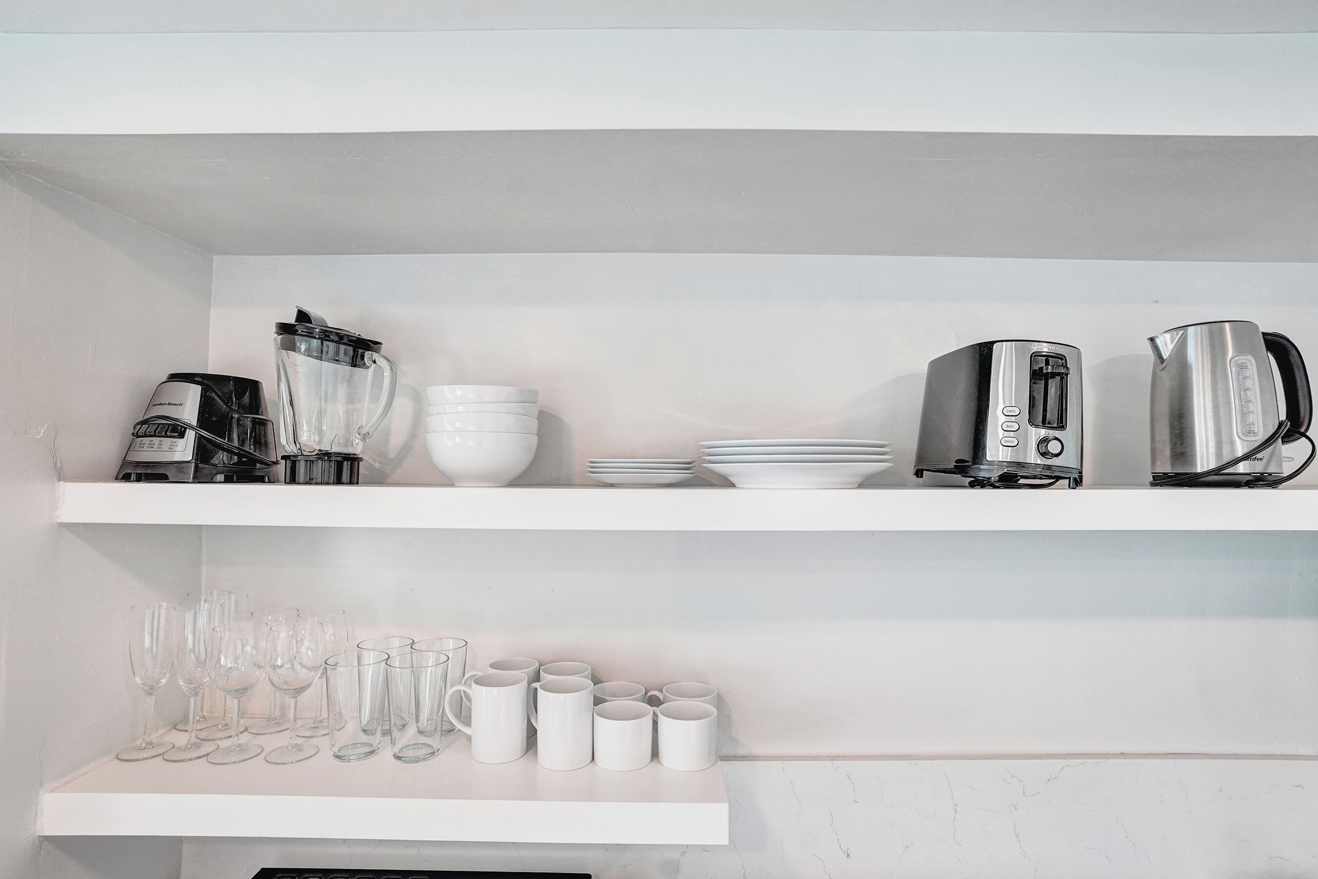 Cozinha com prateleiras brancas, cafeteira, torradeira e diversos copos.