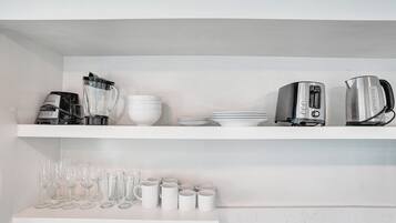 Cozinha com prateleiras brancas, cafeteira, torradeira e diversos copos.