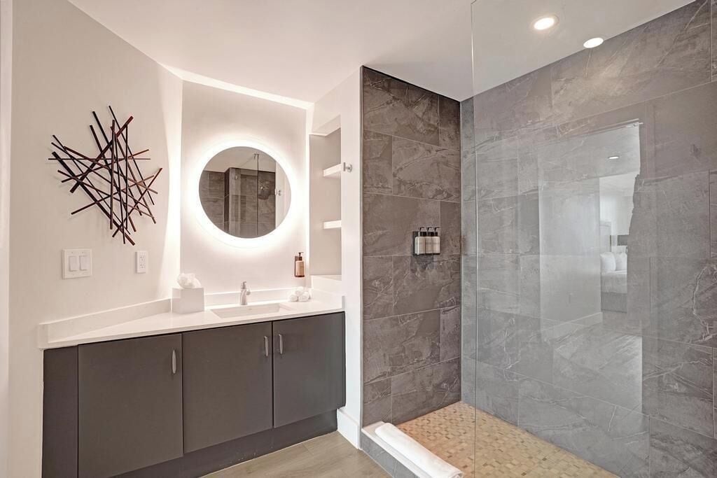 Une salle de bain moderne avec un grand miroir rond, des meubles sombres et une douche à parois de verre.