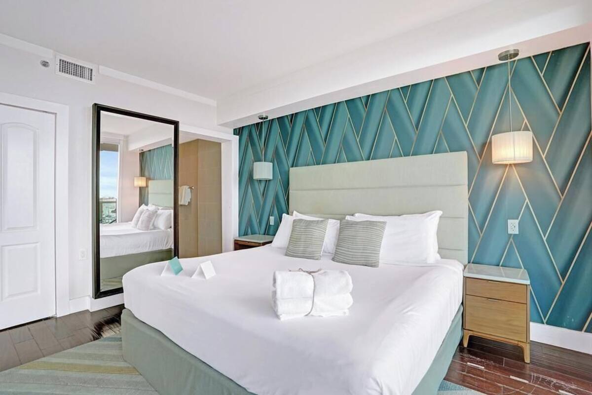 A hotel room with a large bed, a mirror, a nightstand, and a wall with a geometric pattern.