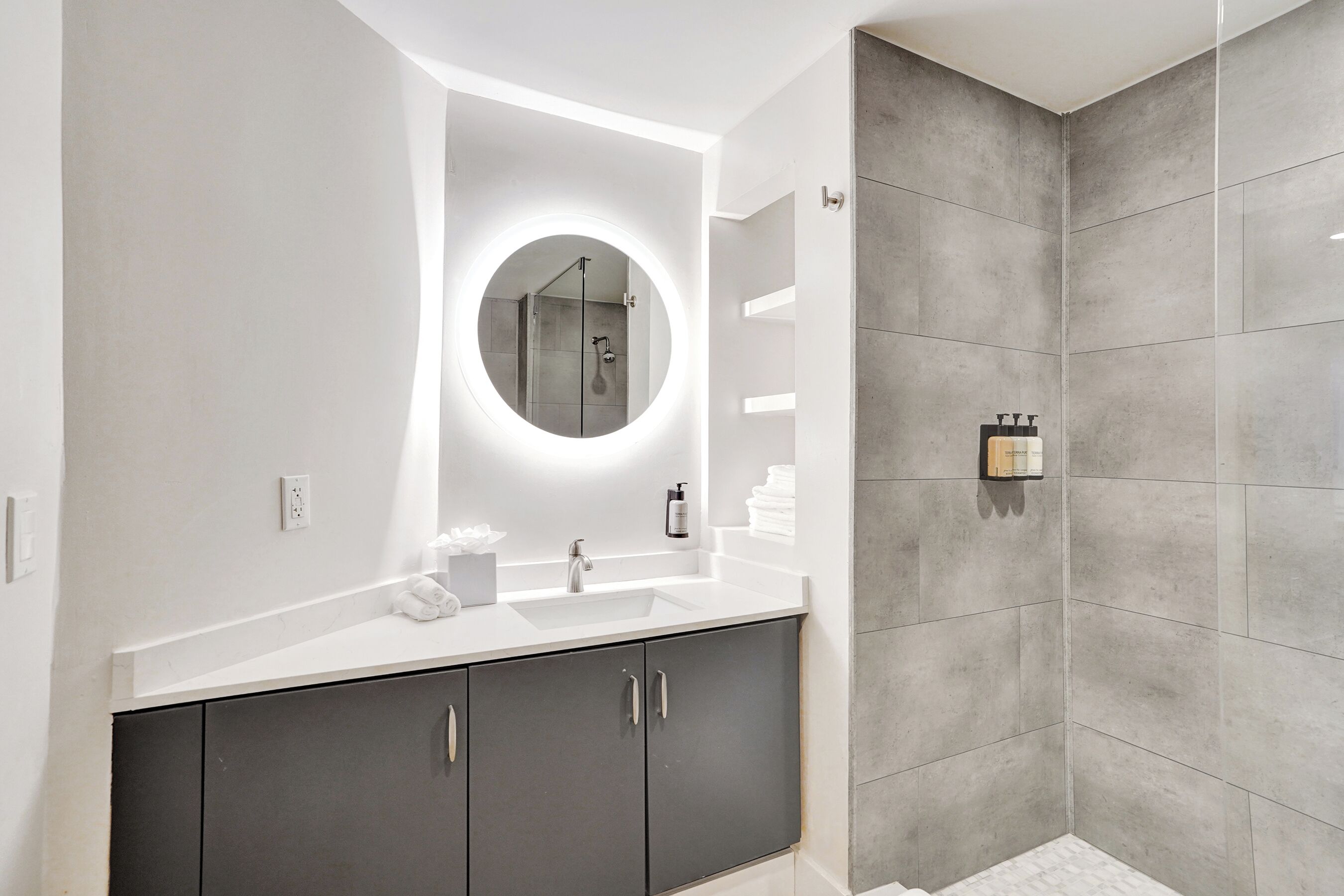 A modern bathroom with a round mirror, a sink, and a shower area.