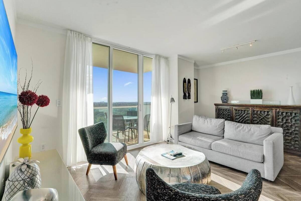A modern living room with a sofa, armchairs, a coffee table, and a view through large glass doors.