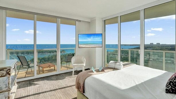 Ein modernes Hotelzimmer mit einem großen Bett, einem Fernseher, einem Balkon mit Meerblick und einer Sitzecke.