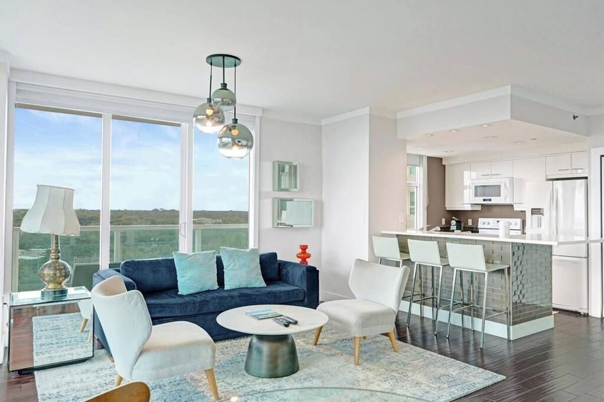 A modern living room with a sofa, chairs, a coffee table, and a kitchen area with white cabinets and appliances.