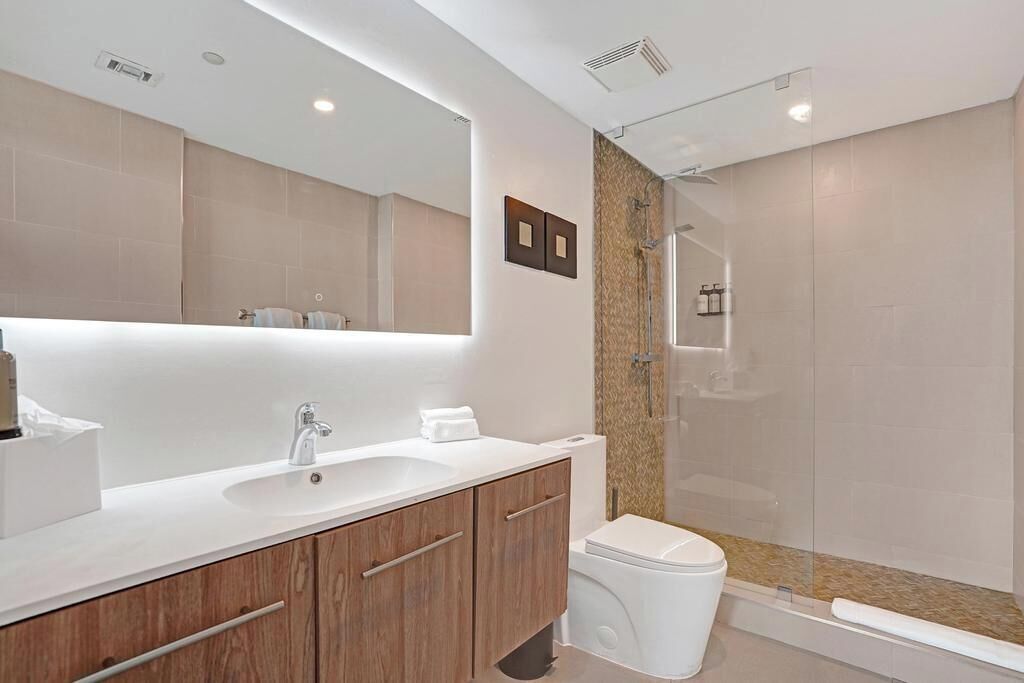A modern bathroom with a large mirror, a sink, a toilet, and a shower area.
