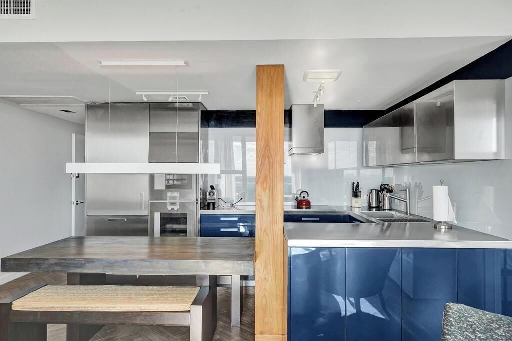 A modern kitchen with stainless steel appliances, a wooden column, and blue cabinetry.