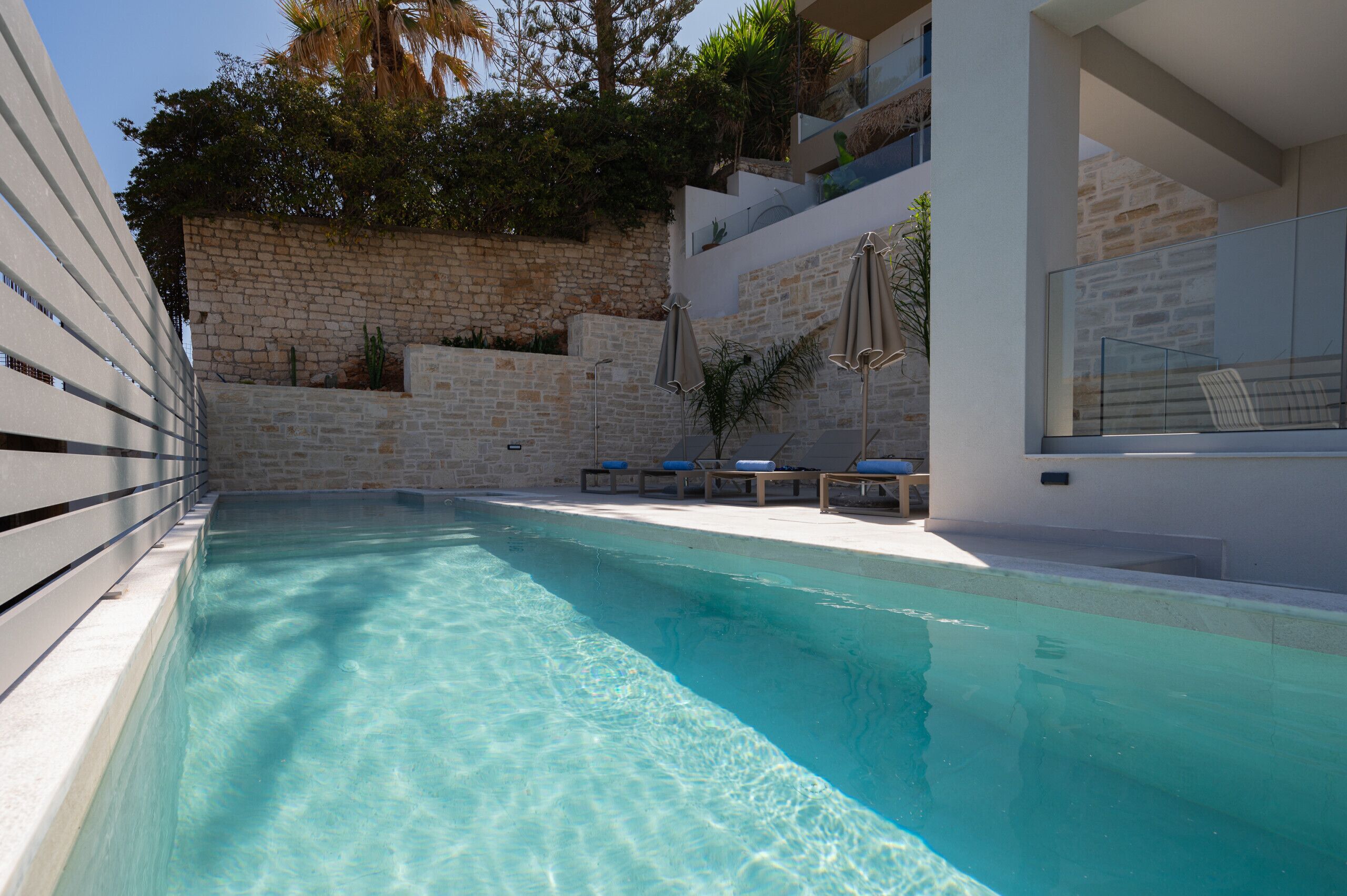 Una piscina con agua cristalina, rodeada de muros de piedra y sillones de descanso modernos.