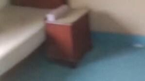 Une petite pièce faiblement éclairée, avec un lit simple et une petite table.
