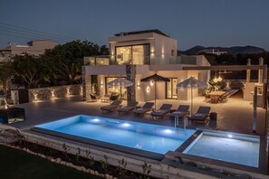 A modern poolside area with lounge chairs, umbrellas, and a swimming pool. - Nysa Luxury villa 1 (Hersonissos)