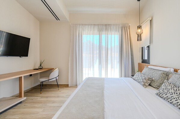 Un dormitorio moderno con cama, escritorio, silla, televisor y ventana con cortinas.