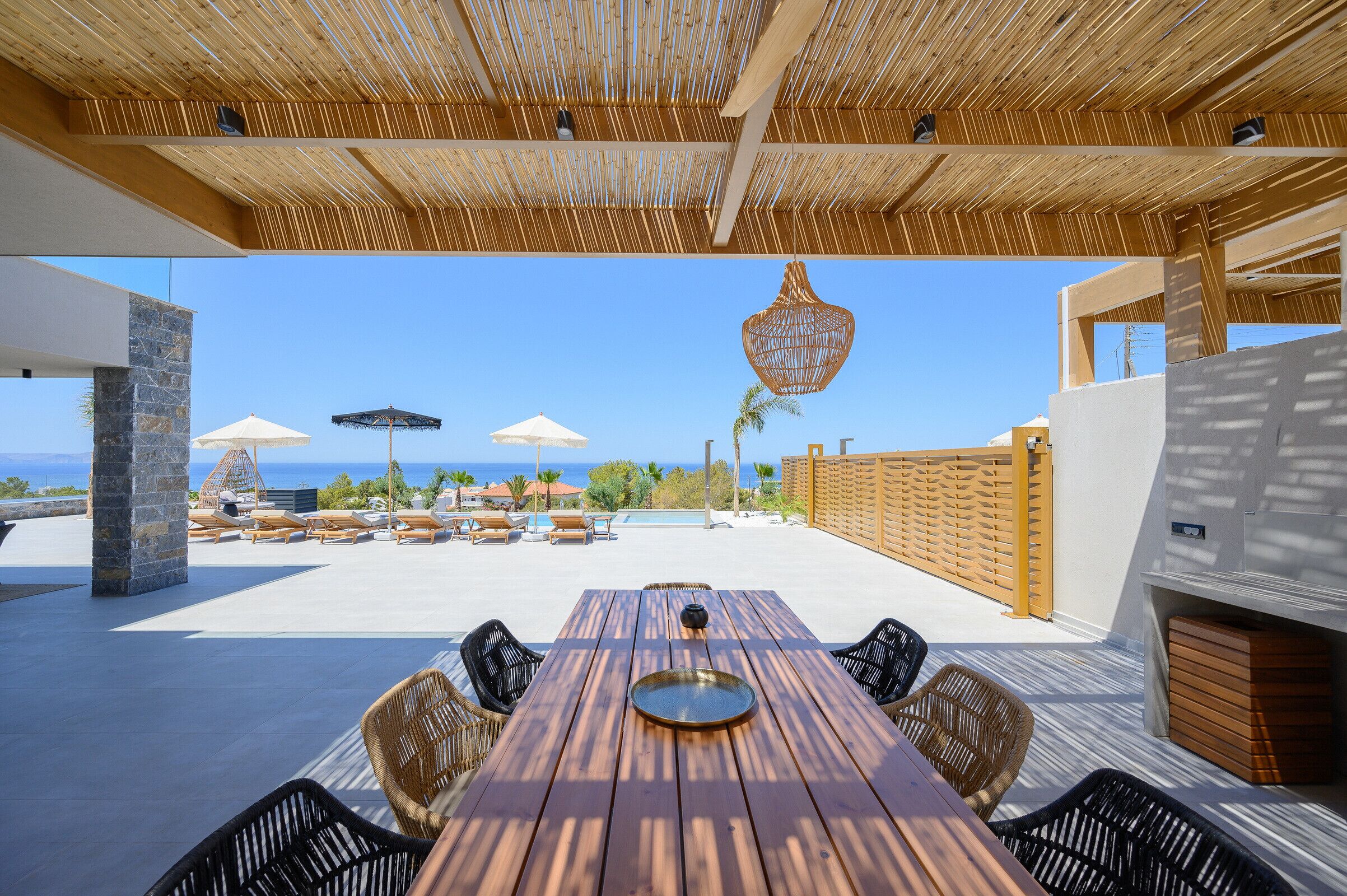 An outdoor patio with a wooden table and chairs, a pool area with lounge chairs, and a view of the ocean.