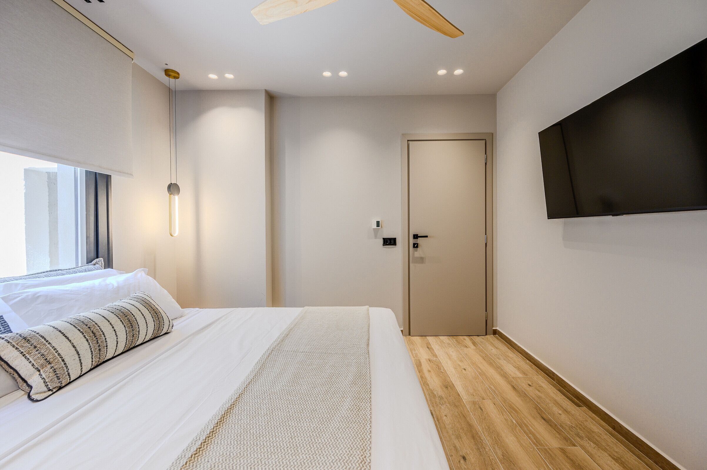 Una habitación de hotel moderna con una cama grande, un televisor de pantalla plana montado en la pared, suelo de madera y una puerta con manija.