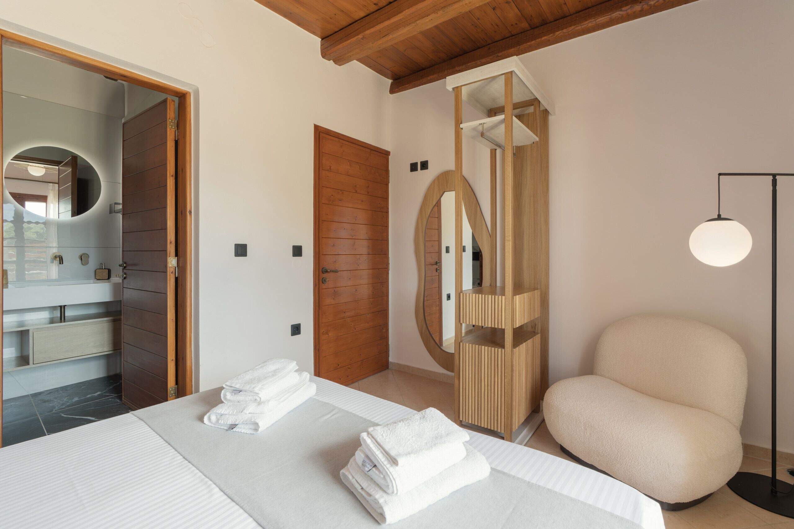 A bedroom with a bed, a wooden door, a mirror, and a bedside lamp.