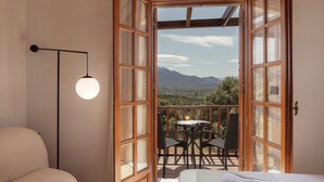 Een kamer met een bed, een ronde tafel met stoelen en een balkon met uitzicht op de bergen.