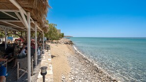 A beachside café with outdoor seating, a thatched roof, and a rocky shoreline. - Petrina Villa 3 (Viannos)